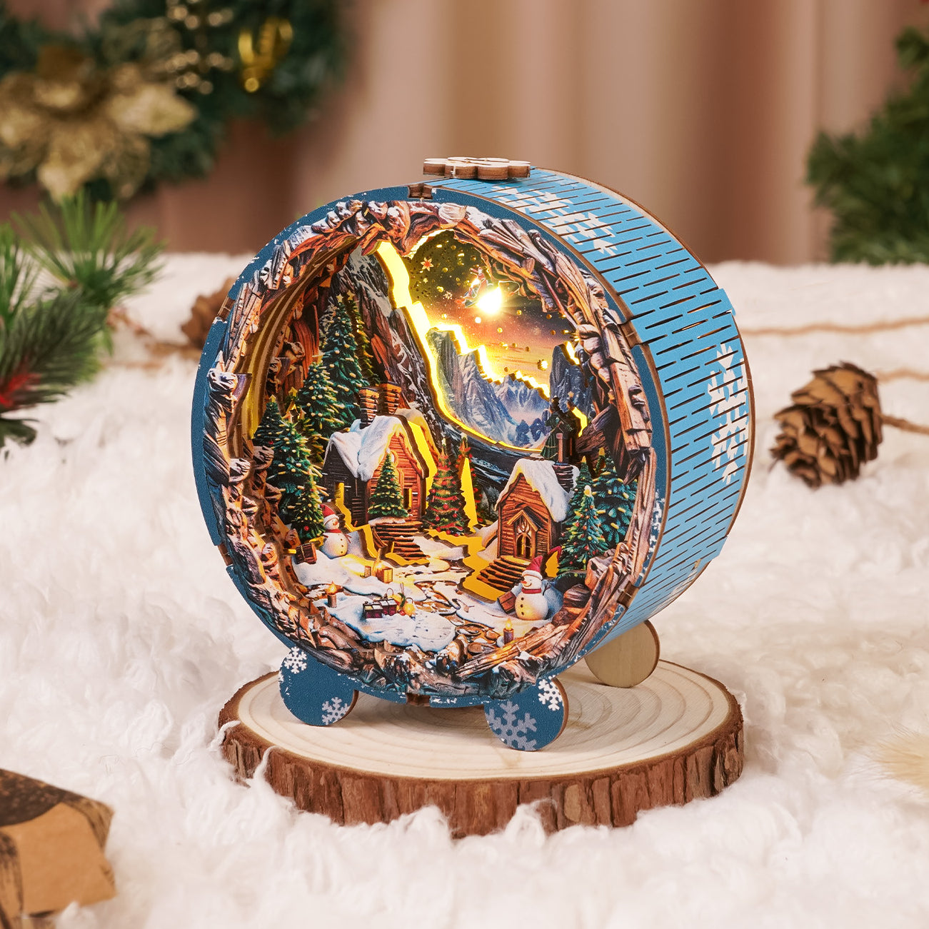 3D wooden Christmas village night light featuring miniature cabins and snow-covered mountains, displayed on a wooden base.
